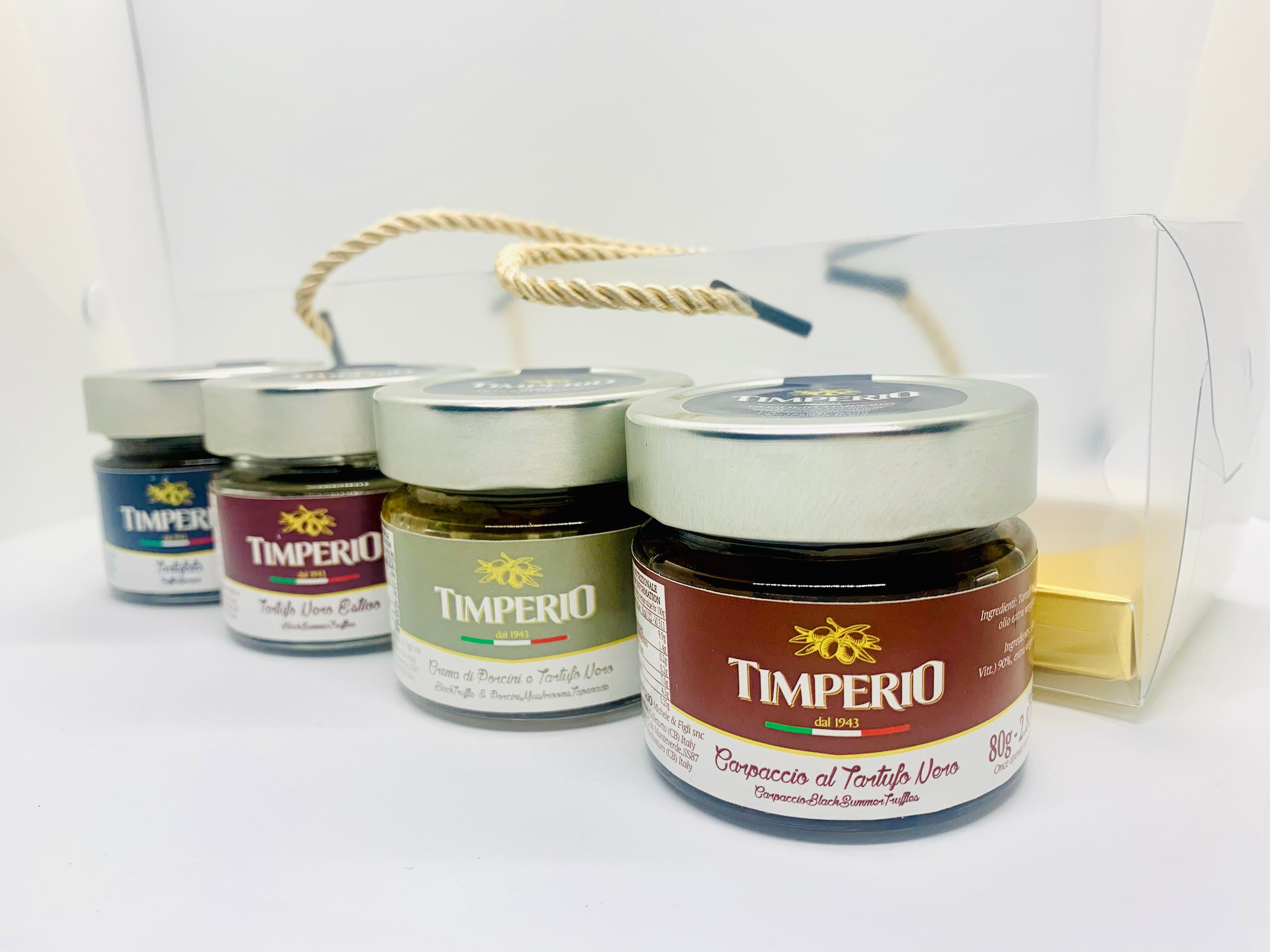 Four jars of Timperio spreads arranged in a clear gift box with a gold rope handle on a white background.